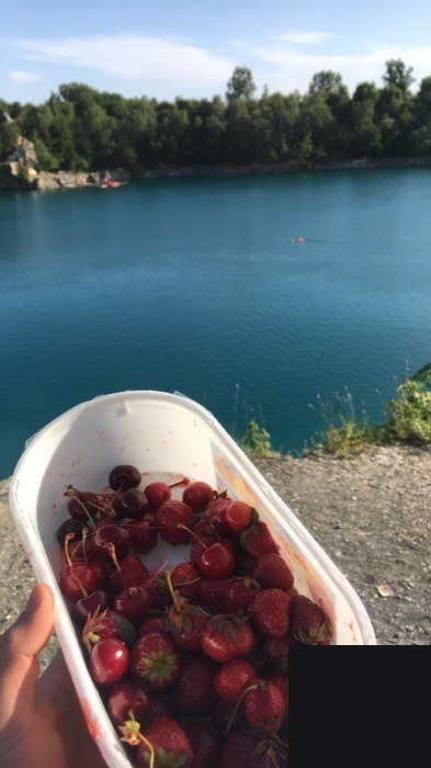 Tub of strawberries and cherries held over turquoise Zakrzowek lake