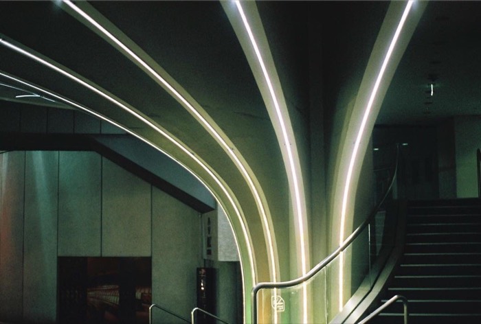 Neon light strips sweeping over curved concrete stairwell architecture, 35mm