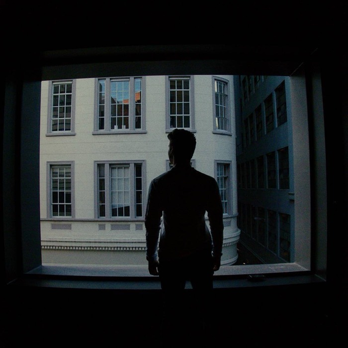 Joshua: moody silhouette self-portrait at dark window facing white building