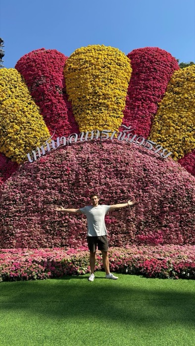 Joshua: arms outstretched before giant flower sculpture with Thai sign