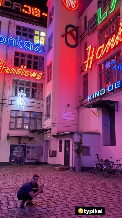 Joshua: crouching beneath glowing vintage neons, Neon Side courtyard at night