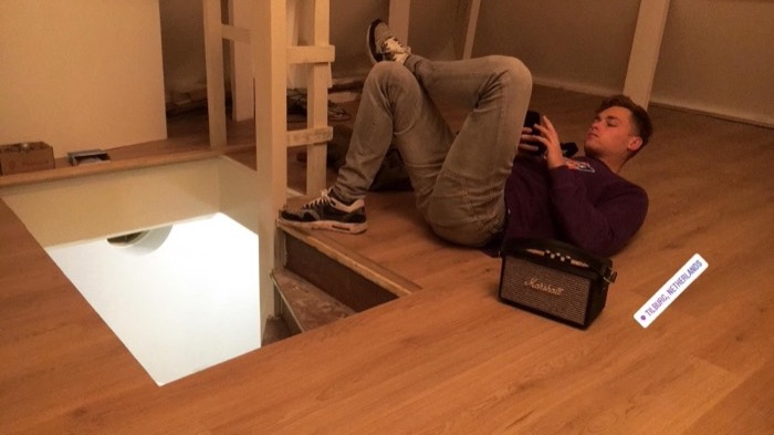 Friend slouched on stairs floor with Marshall speaker, rotated casual shot