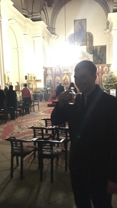 Joshua: grinning with beer inside ornate Orthodox church, Christmas tree behind