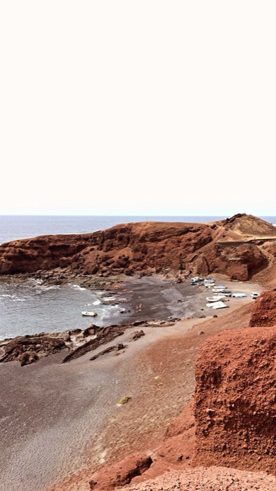 Red volcanic cliffs and black-sand cove with fishing boats
