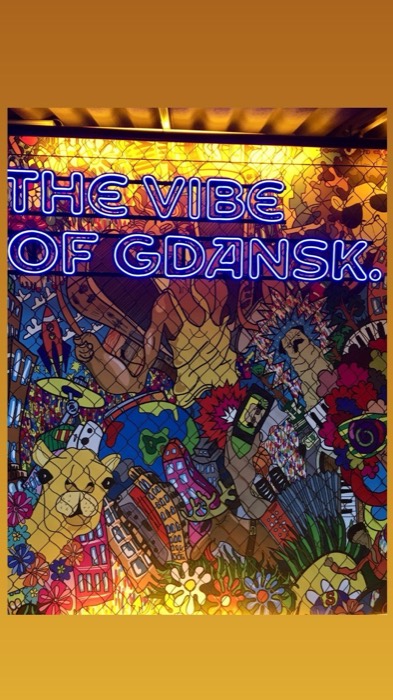 Blue neon 'The Vibe of Gdansk' over colorful stained-glass mural