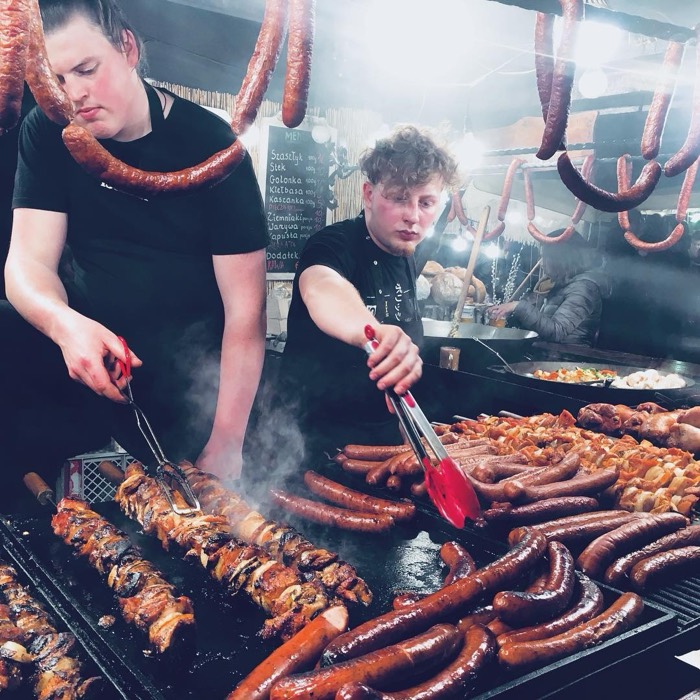 Cooks tonging sausages at Krakow Easter market grill, kielbasa hanging overhead