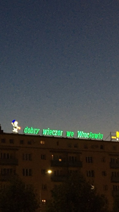 Iconic green neon 'dobry wieczor we Wroclawiu' glowing on rooftop at dawn