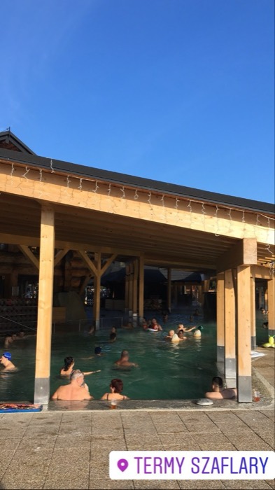 Outdoor thermal pools under wooden canopy, bathers in winter sun
