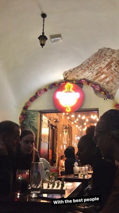 Friends with chess and drinks under neon sign in brick-arched bar