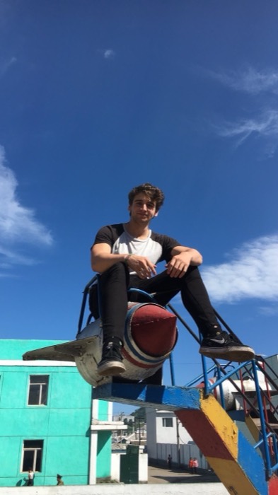 Joshua: sitting atop rocket-shaped playground ride, NK soldier below, blue sky