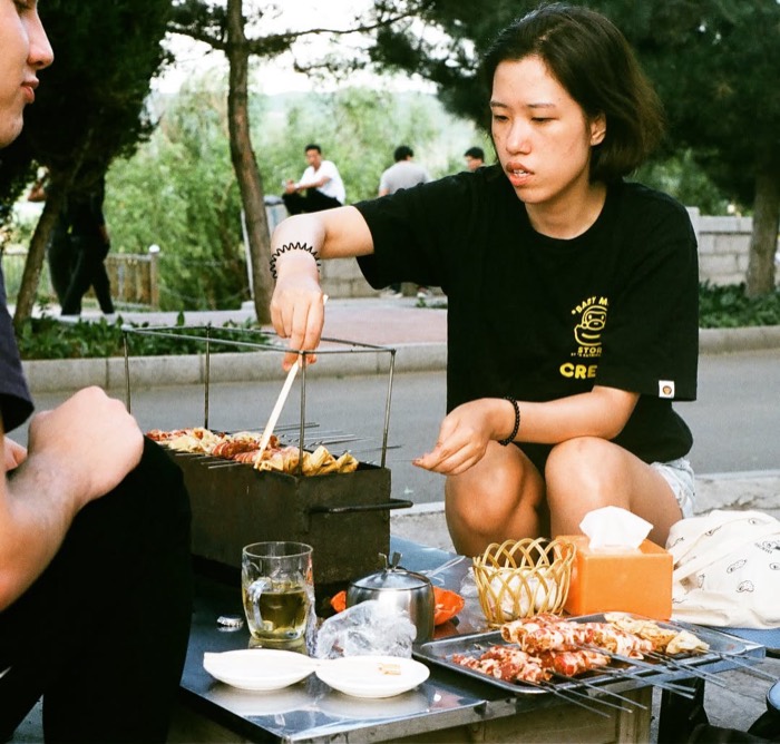 35mm portrait of woman grilling skewers at riverside Korean BBQ