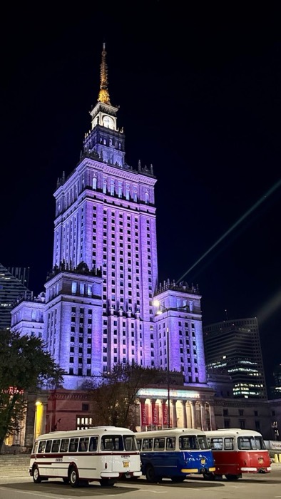 Palace of Culture lit purple at night, three vintage Jelcz buses