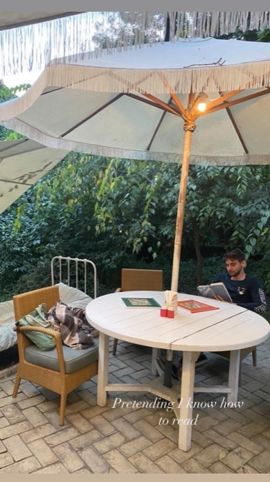 Joshua: reading a book under fringed umbrella in leafy courtyard cafe