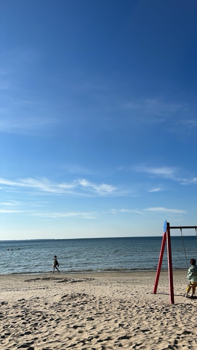 Baltic beach with red swing set, swimmers and walker, blue sky