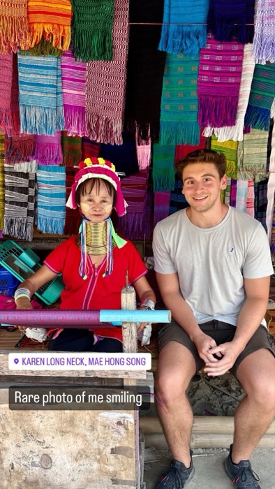 Joshua: smiling beside Karen long-neck weaver among colourful textiles