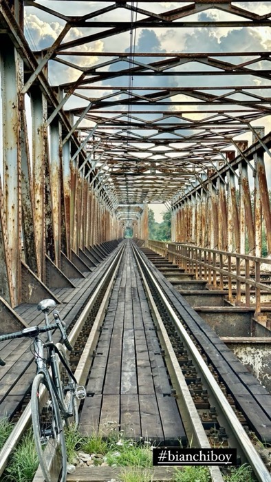 Bianchi bike leaning on rusty railway truss bridge, rails receding