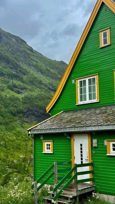 Vivid green wooden house with yellow trim under misty fjord mountainside