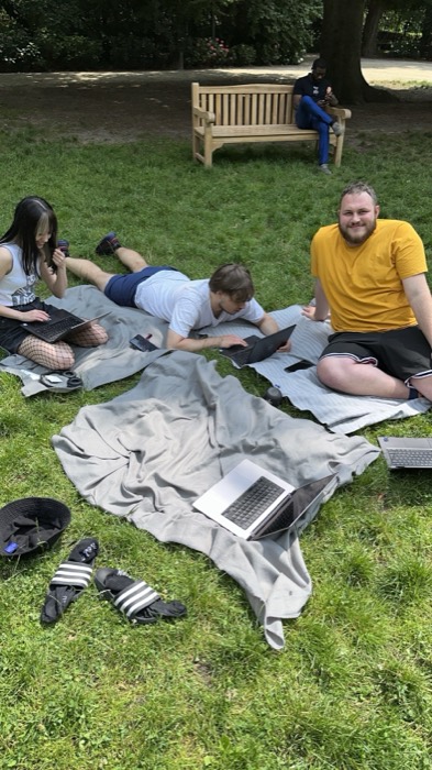 Colleagues working on laptops on a blanket in a park