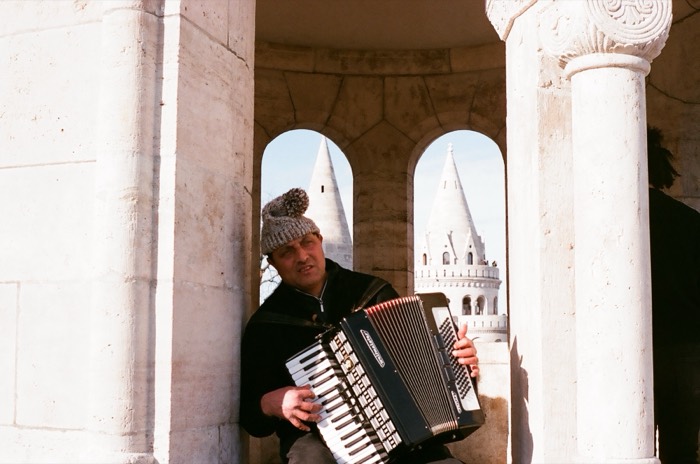Accordion busker at Fishermans Bastion white turrets, sunny day.