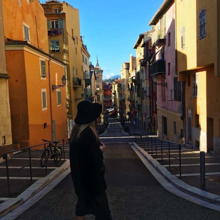 Woman in black hat on sunlit colourful old-town street, hilltop chapel