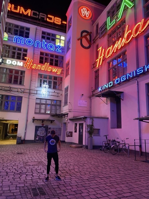 Joshua: in neon-sign courtyard, Montaz Hanka Kino Ognisko glowing