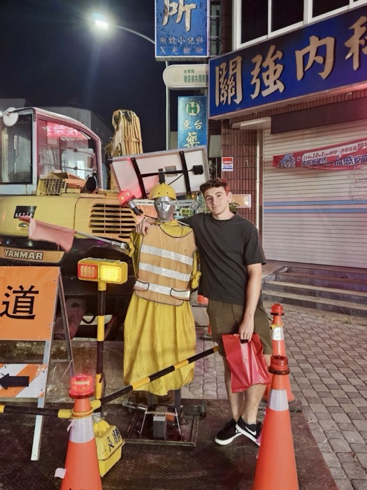 Joshua: posing arm-around quirky high-vis roadwork mannequin beside crane at night