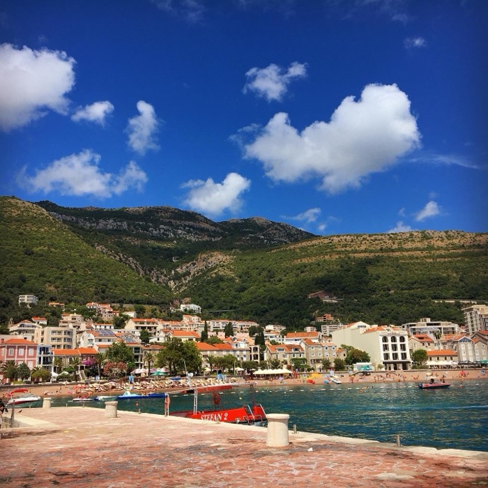 Coastal town beneath green mountains, turquoise sea, beach promenade