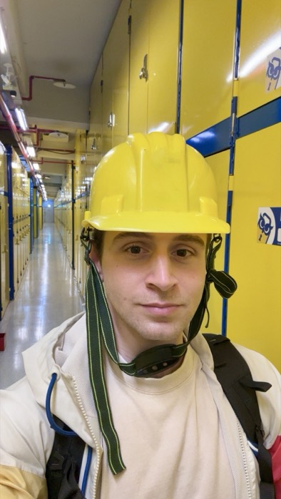 Joshua: selfie in a yellow hard hat inside an industrial corridor