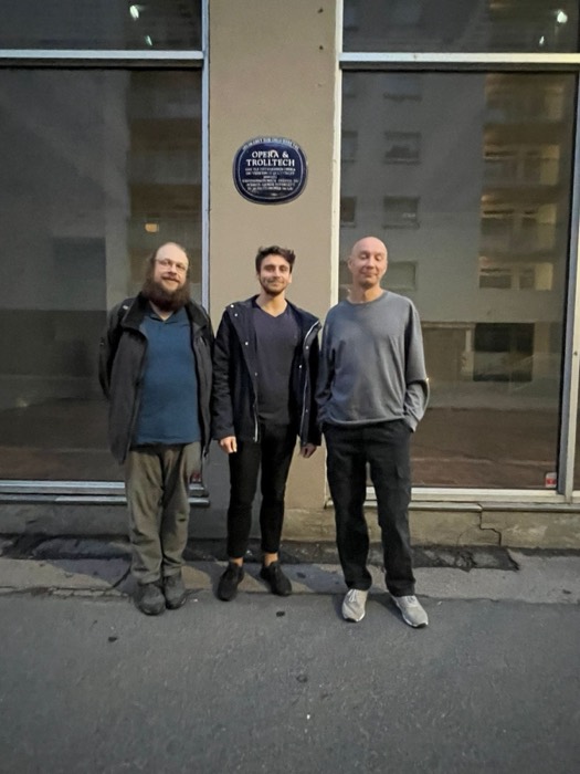 Joshua: with two friends under 'Opera & Trolltech' blue plaque, tech history.