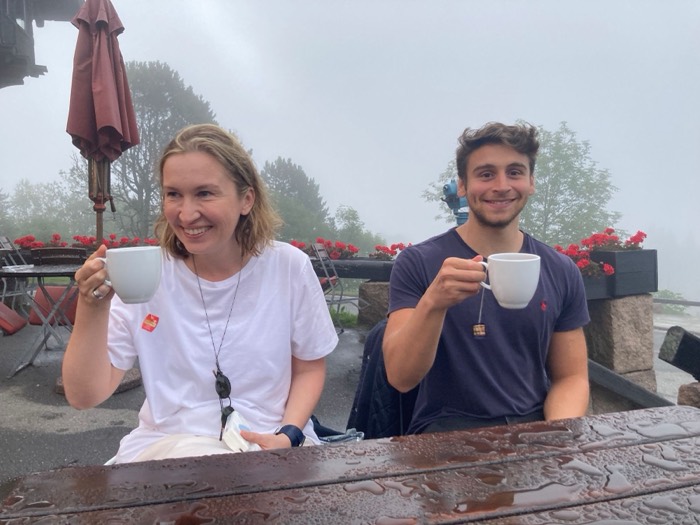 Joshua: toasting tea mugs with woman at foggy mountain cafe terrace