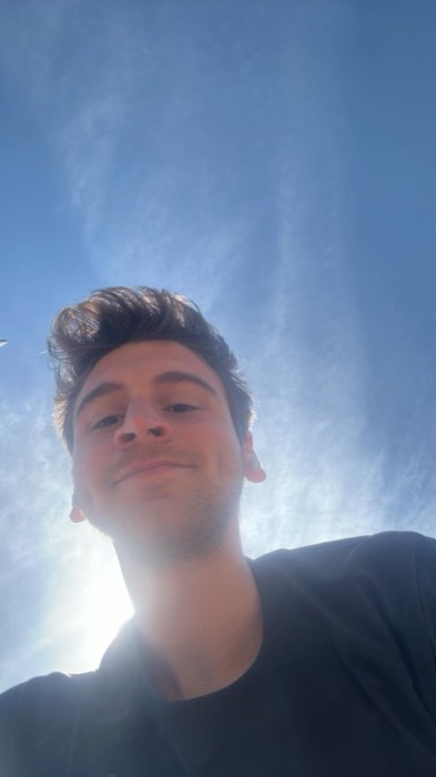 Joshua: low-angle sun-flared selfie against blue sky, slight squint
