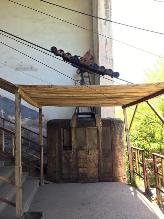 Rusted Soviet cable-car cabin arriving at bamboo-roofed station