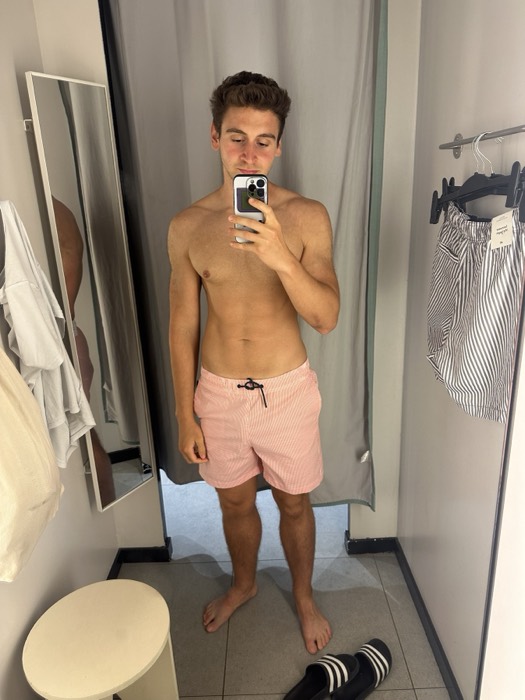 Joshua: trying pink swim shorts in a fitting room mirror