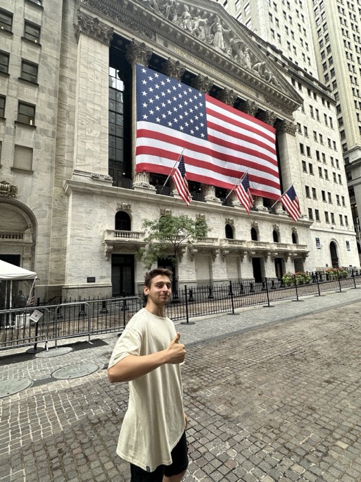 Joshua: thumbs up in front of flag-draped New York Stock Exchange.