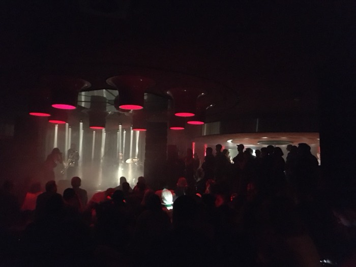Atmospheric red-lit club, band on stage in haze