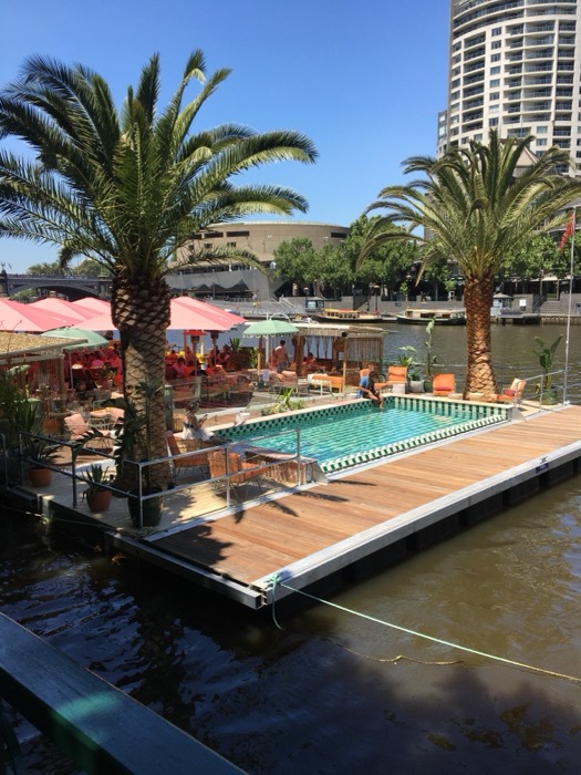 Floating pool bar on Yarra River with palms, arts precinct behind