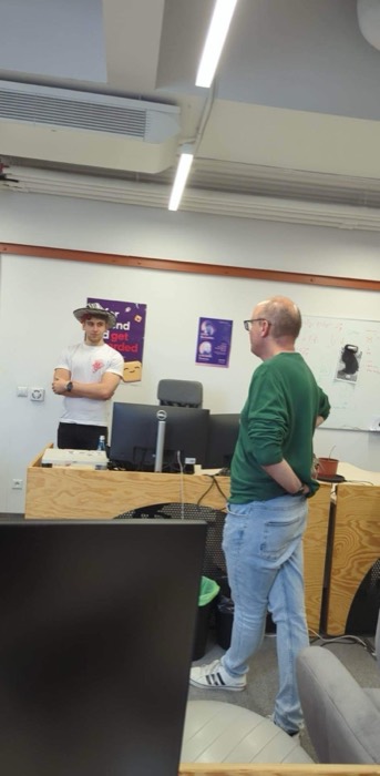 Joshua: in safari hat chatting with colleague in office