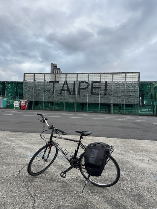 Loaded touring bike parked before pixelated TAIPEI sign, overcast sky