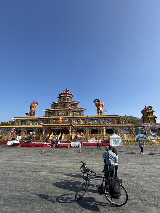 Touring bike and people before huge ornate temple festival structure