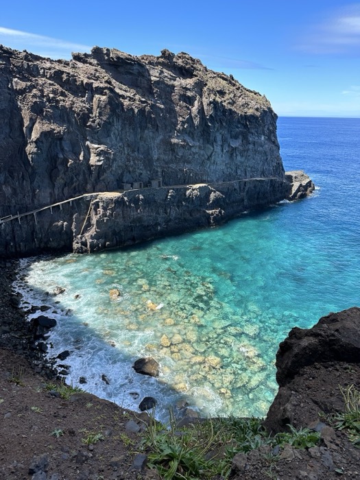 Turquoise natural rock pool against black volcanic cliffs and ocean