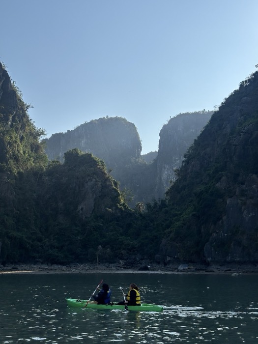 Kayakers paddling beneath misty limestone karst cliffs in Ha Long Bay