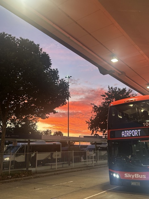 SkyBus airport double-decker under fiery pink-orange sunset sky