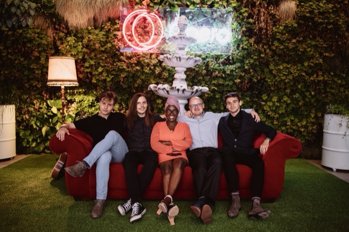 Joshua: far right in group portrait on red couch, Opera event neon backdrop.