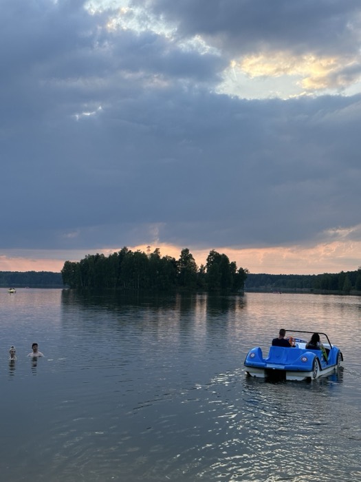 Blue car-shaped pedalo and swimmers on lake at moody sunset