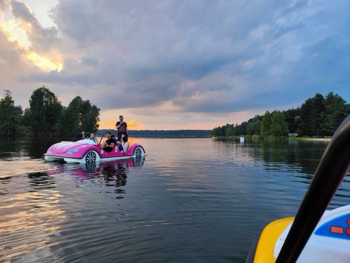 Friends on pink swan pedal-boat at sunset on lake