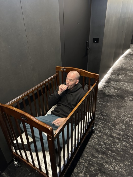 Friend sitting in baby crib in dark hotel corridor