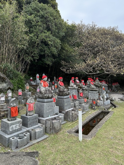 Rows of red-capped stone Jizo statues in a hillside temple garden