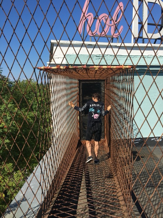 Joshua: walking through caged rope walkway toward pink neon sign