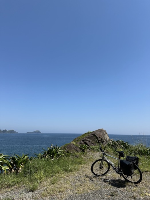 Touring bike on grassy headland above deep blue sea and islets.