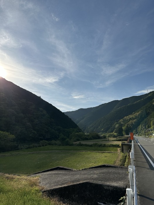 Sunlit mountain valley with rice paddies and roadside, rural Japan cycling